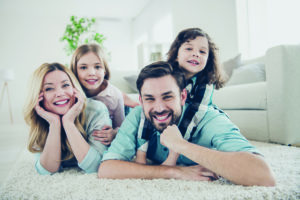 Photo of four members adopted family lying floor toothy smiling fluffy carpet cozy apartments