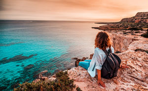 Girl sitting on a cliff with backpack